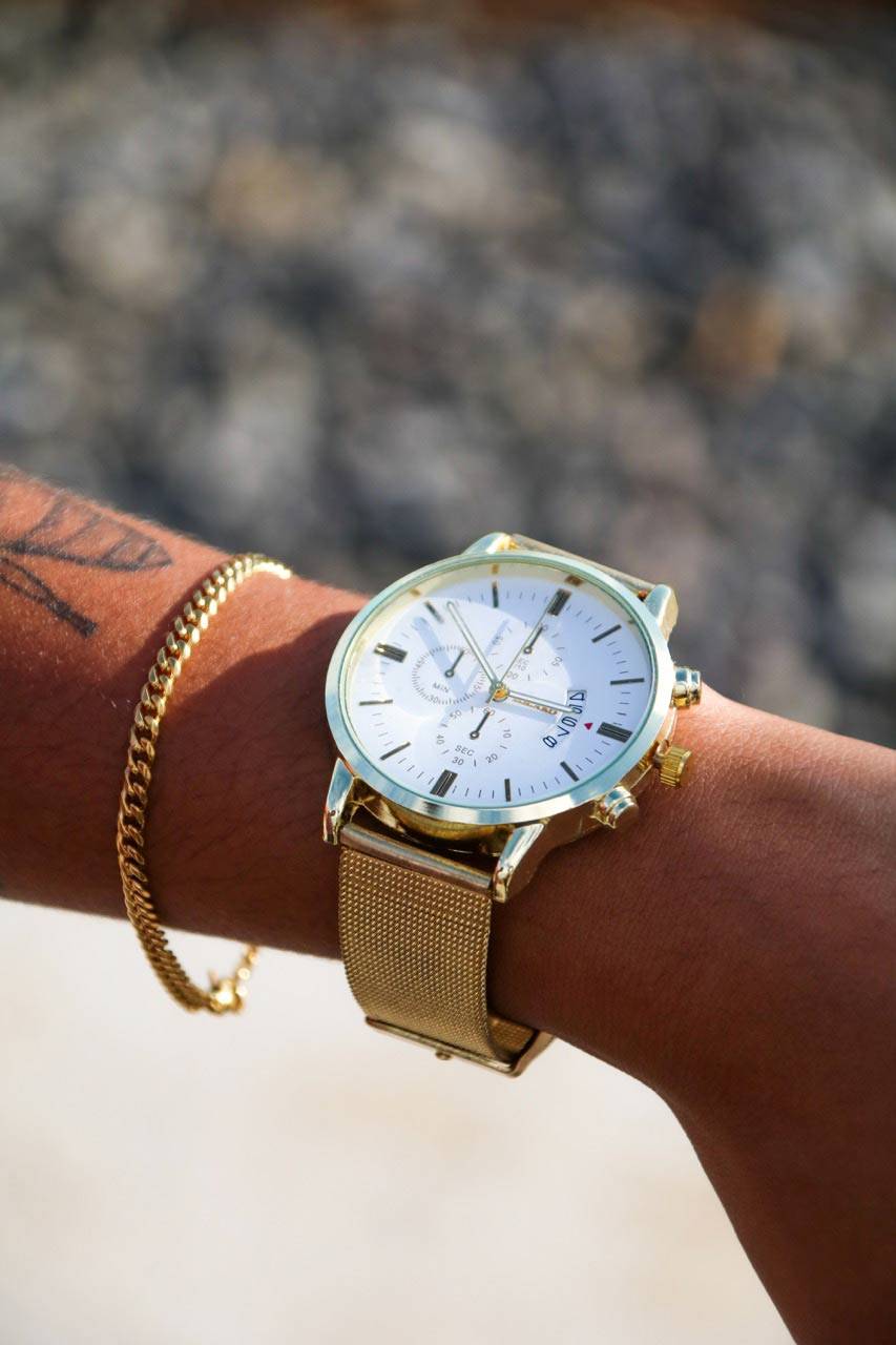 Montre Infinity dorée portée au poignet, cadran blanc et bracelet en acier inoxydable. Élégance et raffinement pour un accessoire de mode intemporel.