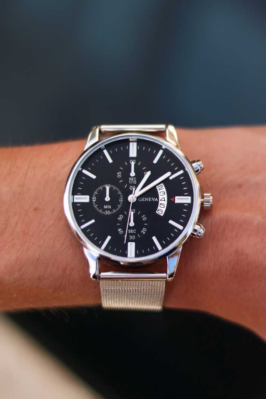 Montre Infinity argentée portée au poignet, cadran noir et bracelet en acier inoxydable. Unisexe, au style moderne et confortable pour un usage quotidien.